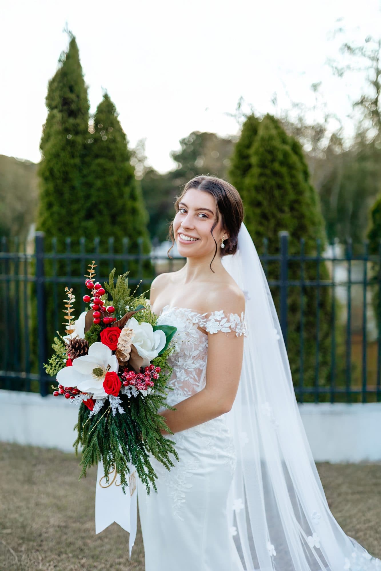 Bre in her wedding gown and veil, holding a winter bouquet of red roses, magnolia and evergreen