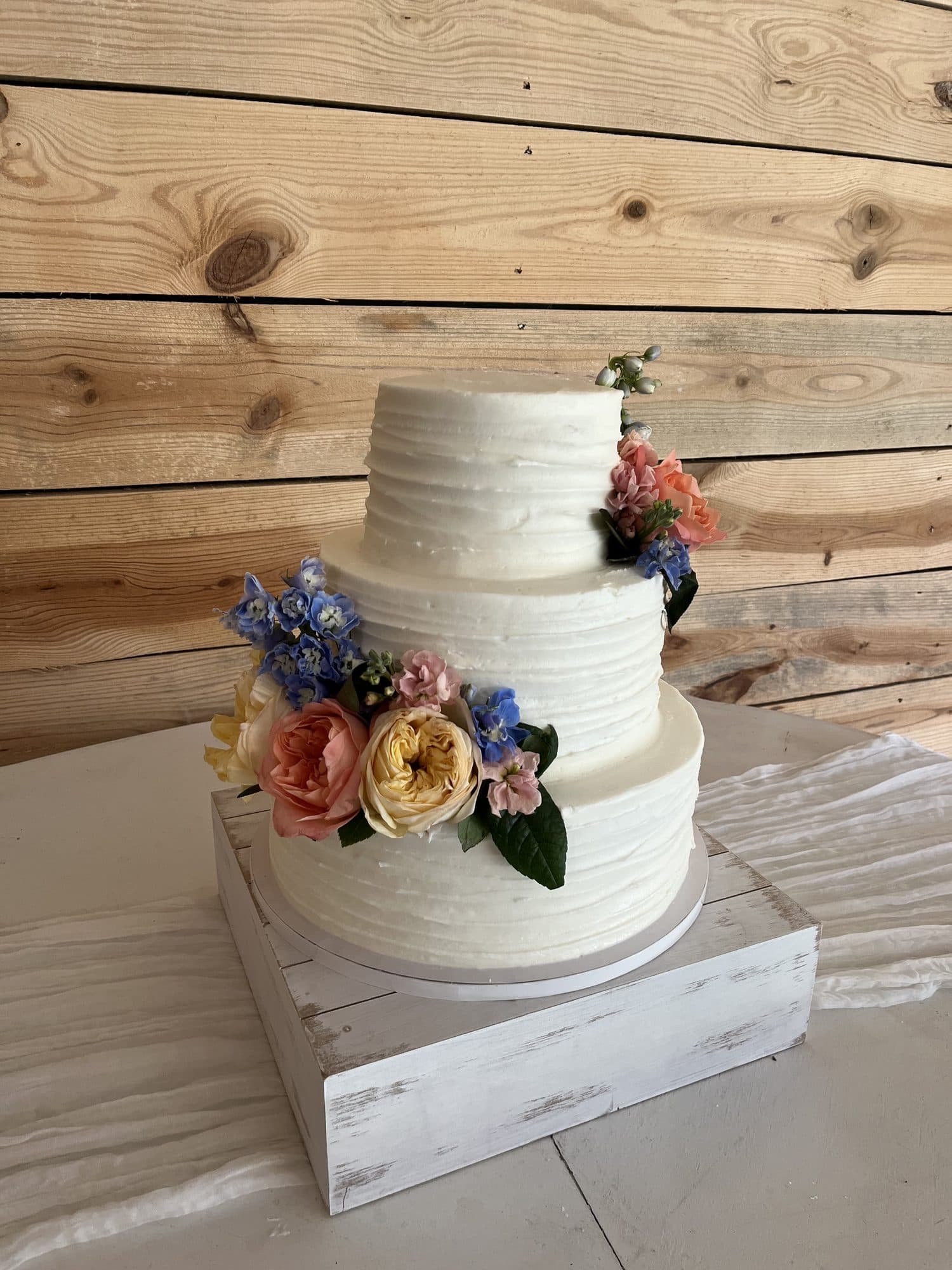 A three-tier buttercream cake dressed with garden roses and blue delphinium